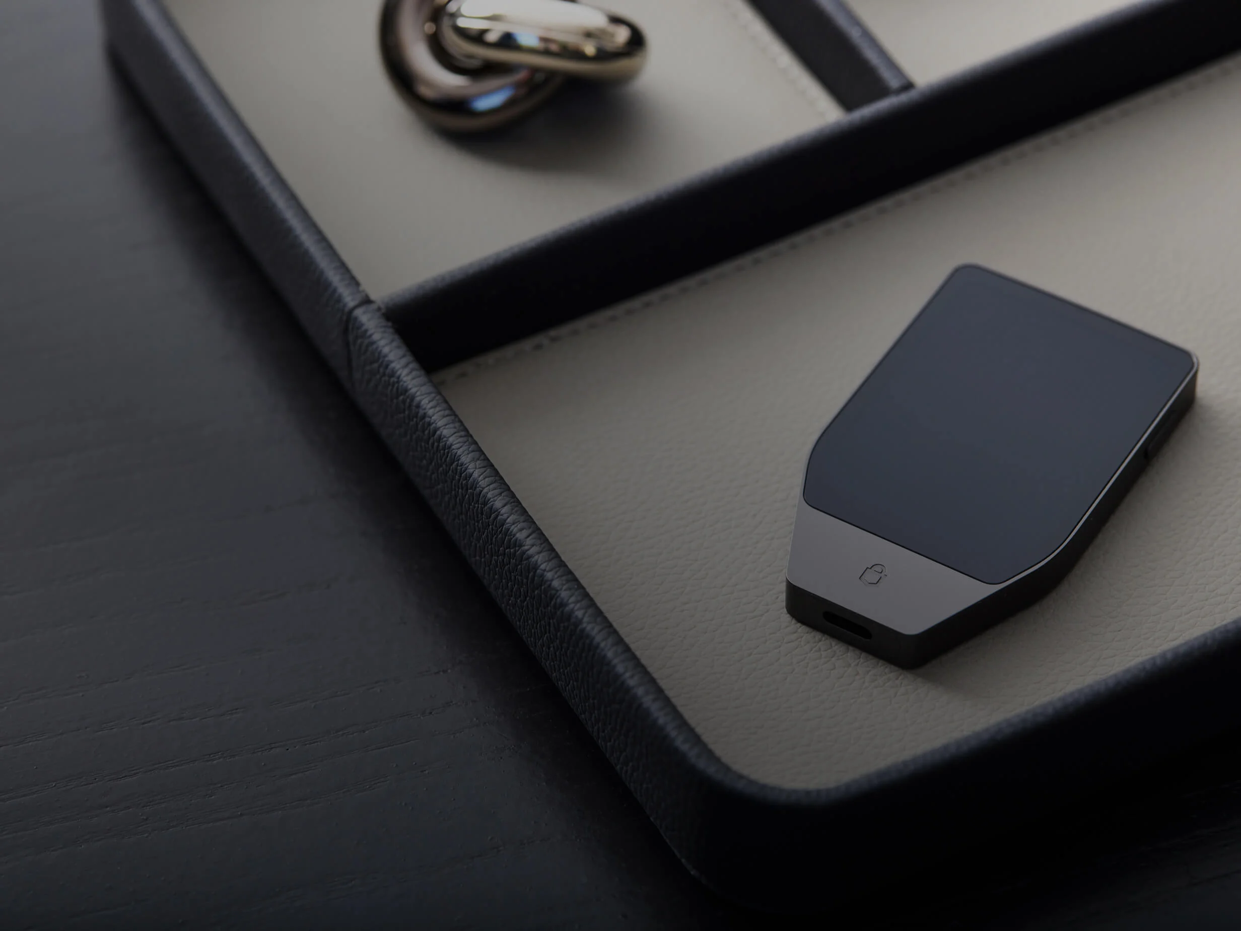 A man sits on a chair using a MacBook while holding a Trezor Safe 7 hardware wallet in one hand.